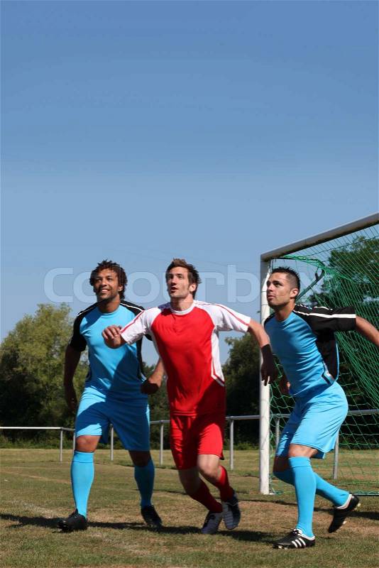 Three footballers waiting for the ball in front of goal, stock photo