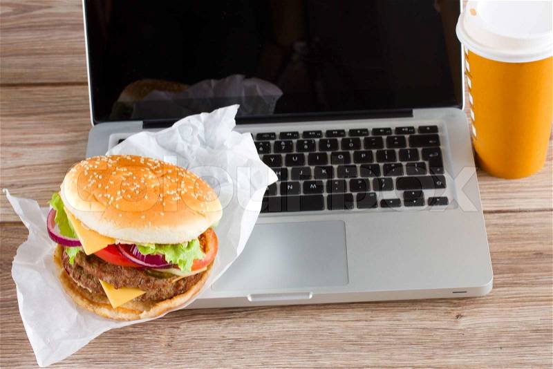 Eating at work place fast food near laptop on wooden table, stock photo