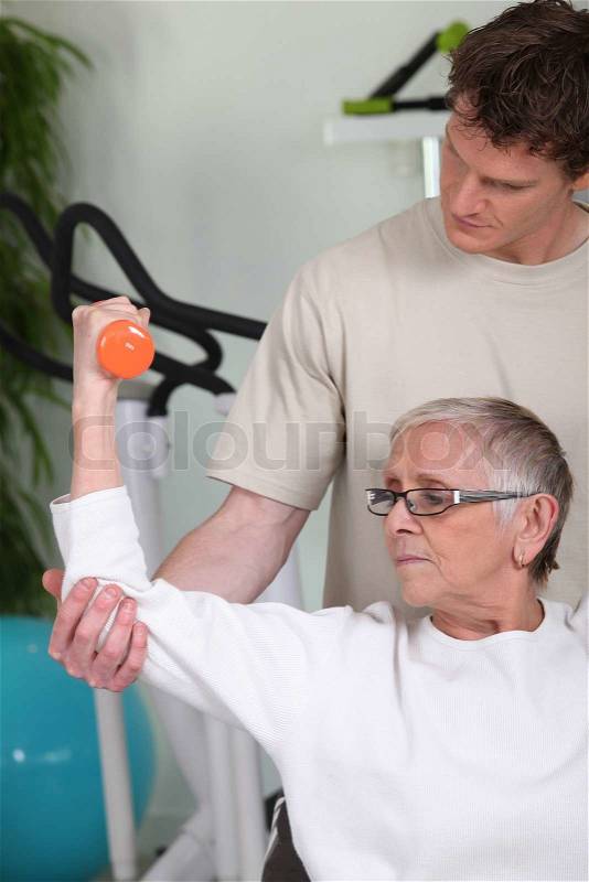 Senior woman lifting dumbbell with fitness coach, stock photo