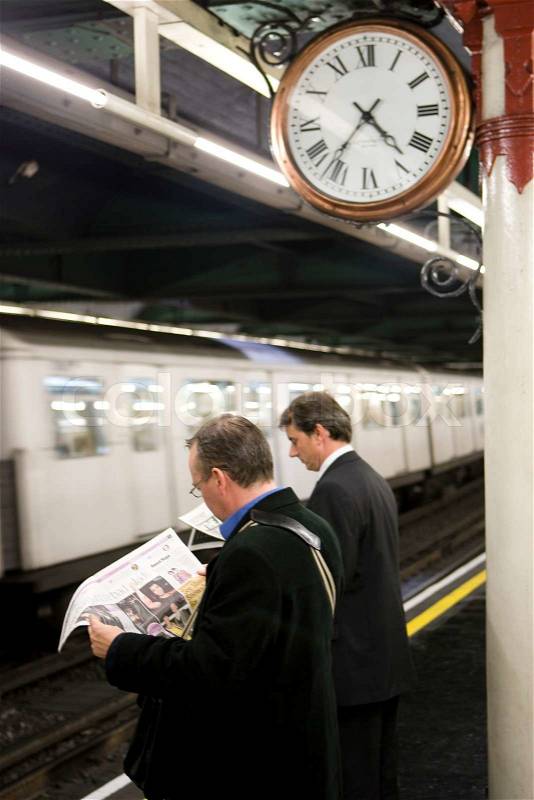 Businessmen reading newspaper while waiting for their train in London underground, stock photo