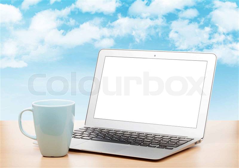 Laptop with blank screen and cup on table over sunny sky background, stock photo