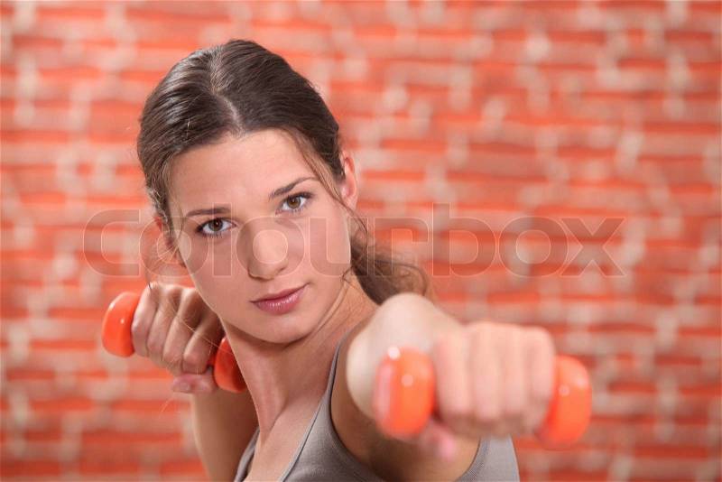 Young woman using hand weights in front of a red brick wall, stock photo