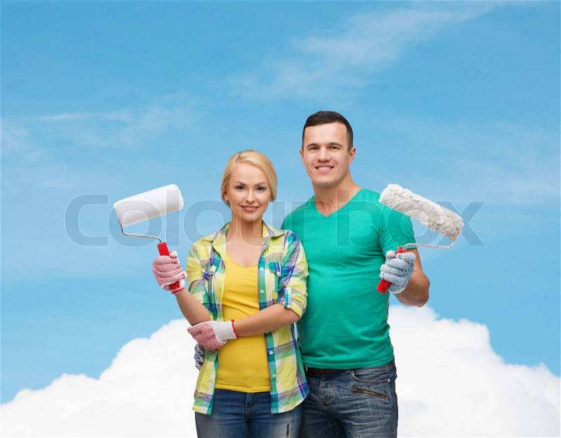 Repair, construction and maintenance concept - smiling couple in gloves with paint rollers, stock photo