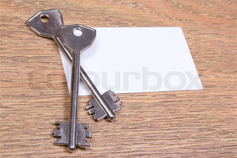 Close up of two metal keys and visiting card on wooden table, stock photo
