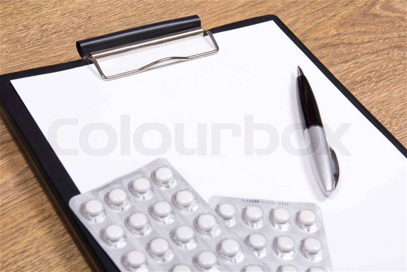 Close up of blank clipboard, pen and pills on wooden background, stock photo