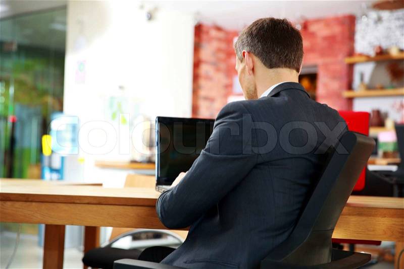 Back view portrait of a businessman sitting with laptop at office, stock photo