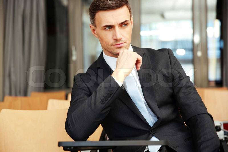 Confident businessman sitting at conference hall, stock photo