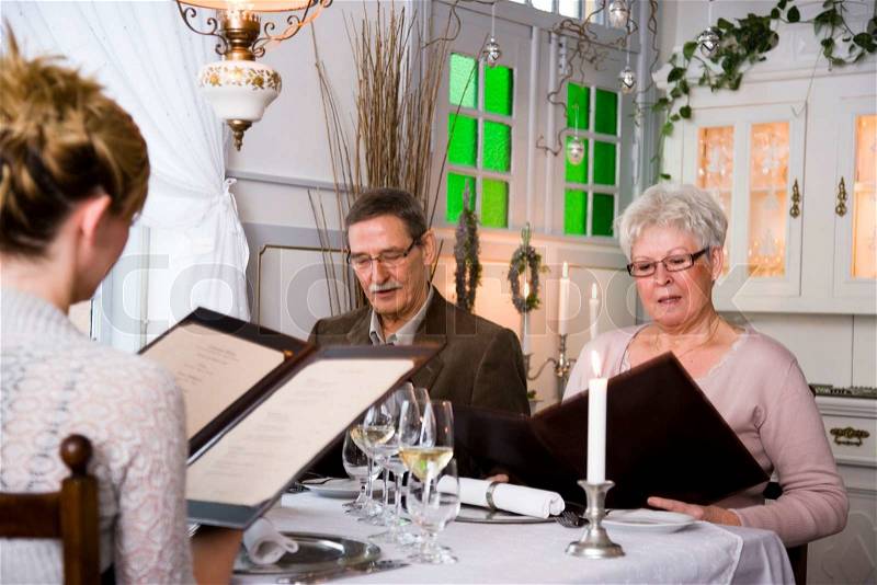 An elderly couple and a woman reading a restaurant\'s menu, stock photo
