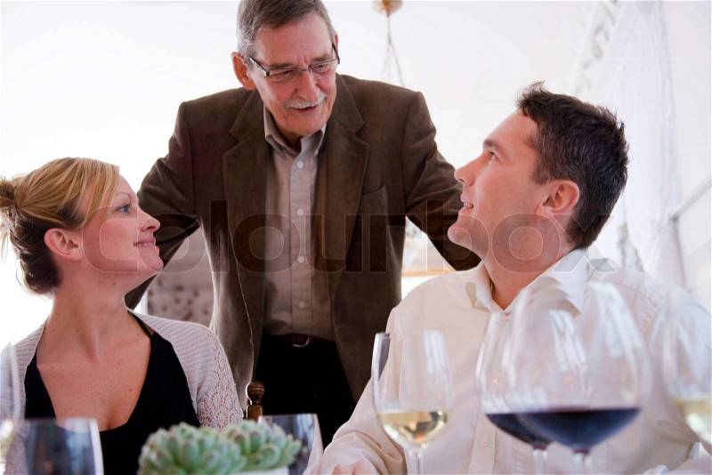 An elderly party host talking to his guests, stock photo