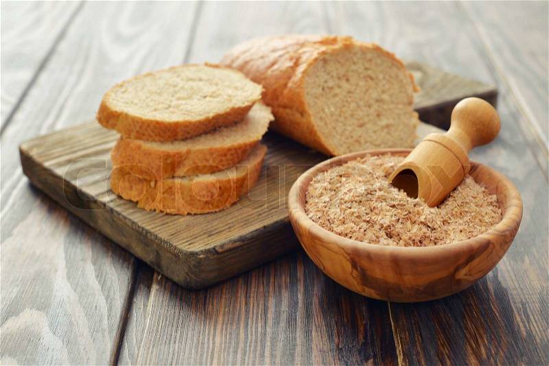 Wheat bran in bowl with sliced bread on wooden background, stock photo