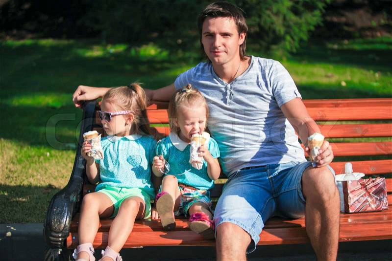 Portrait of two little cute girls and young father eating ice-cream outdoors, stock photo
