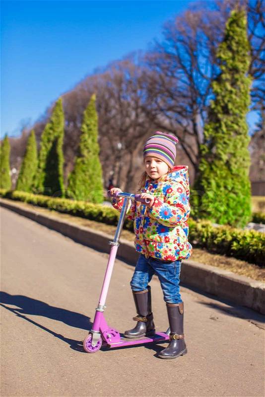 Adorable little girl have fun on the scooter in warm spring day, stock photo