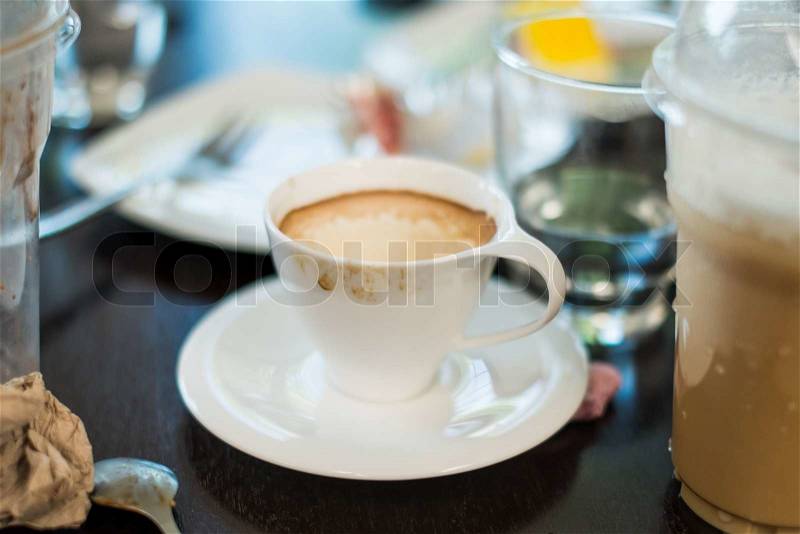 Messy cup of espresso / macchiato surrounded by dessert plate and iced coffee plastic cups on cafe table, stock photo