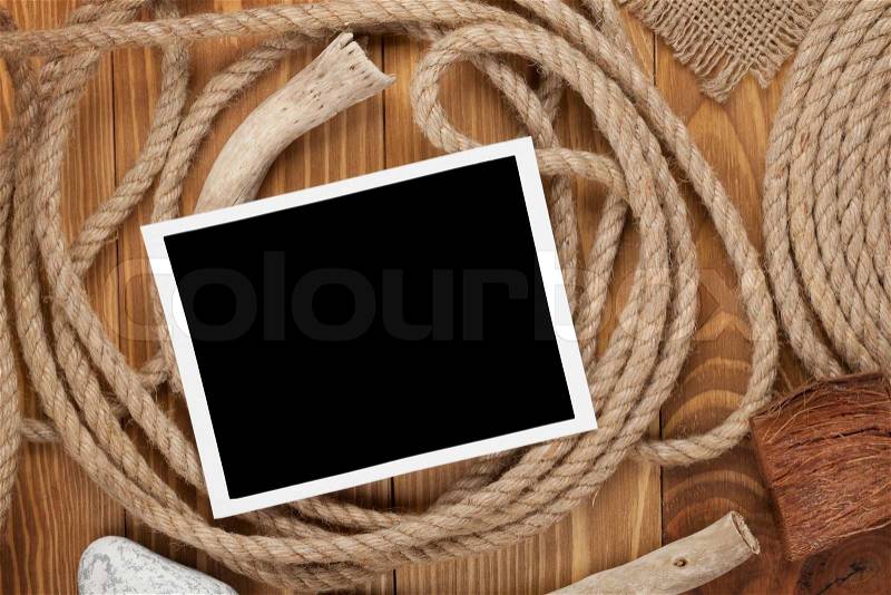 Blank photo frame with ship rope over wooden background, stock photo