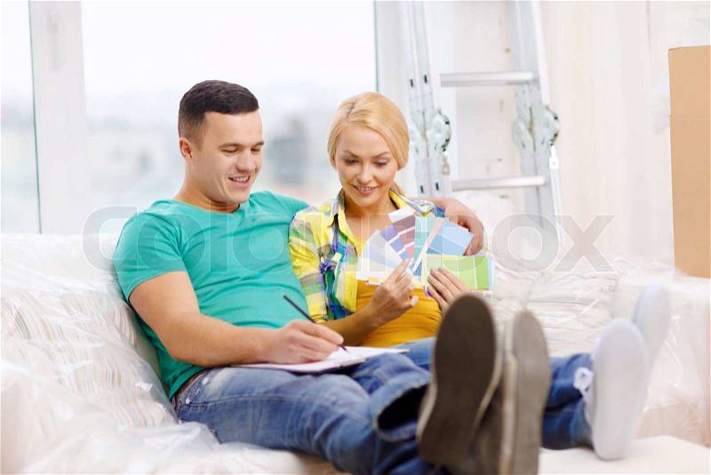 Moving, home and couple concept - smiling couple looking at color samples in new home, stock photo