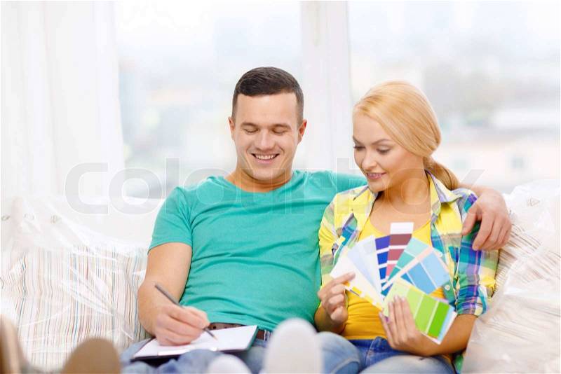 Moving, home and couple concept - smiling couple looking at color samples in new home, stock photo