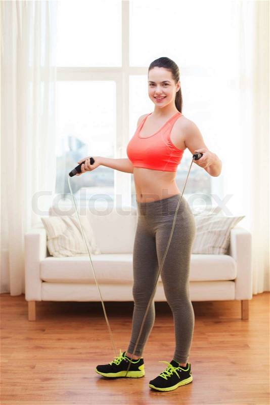 Fitness, home and diet concept - smiling teenage girl with skipping rope at home, stock photo