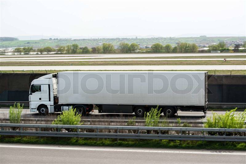 White truck moving on a highway nest to airport runway with space for your company logo and text, stock photo