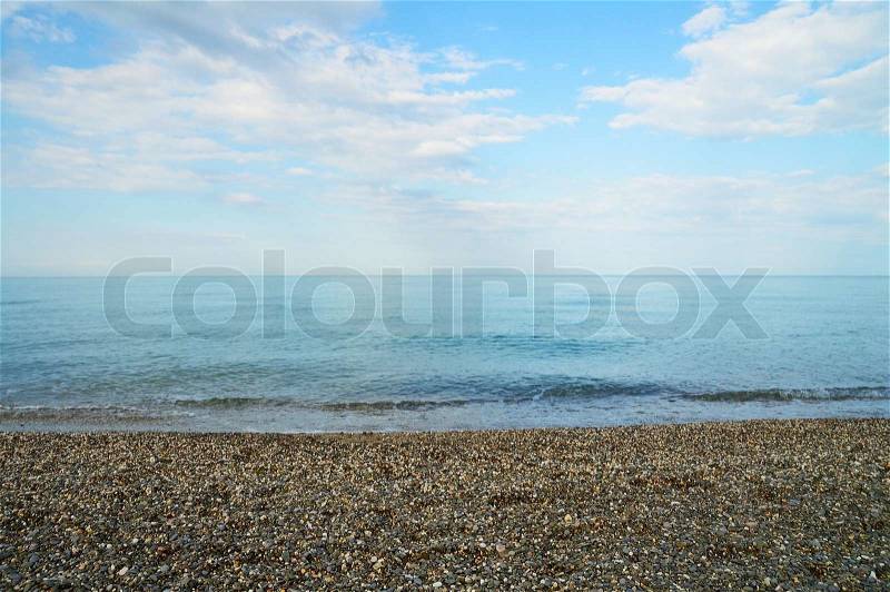 Calm blue sea with pebble coast under light clouds in the sky, stock photo