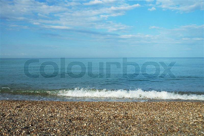 Calm blue sea with pebble coast under light clouds in the sky, stock photo