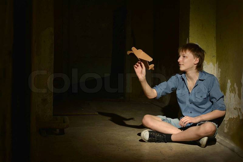 Lonely little boy with paper plane in a dark cellar, stock photo