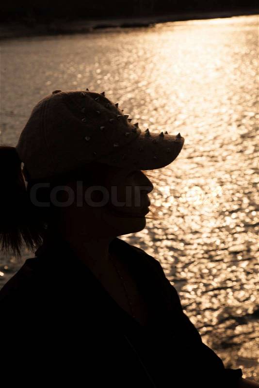 Backlit silhouette of a woman wearing a hat. Sop freckled sunlight reflecting off the surface of the sea in the evening, stock photo