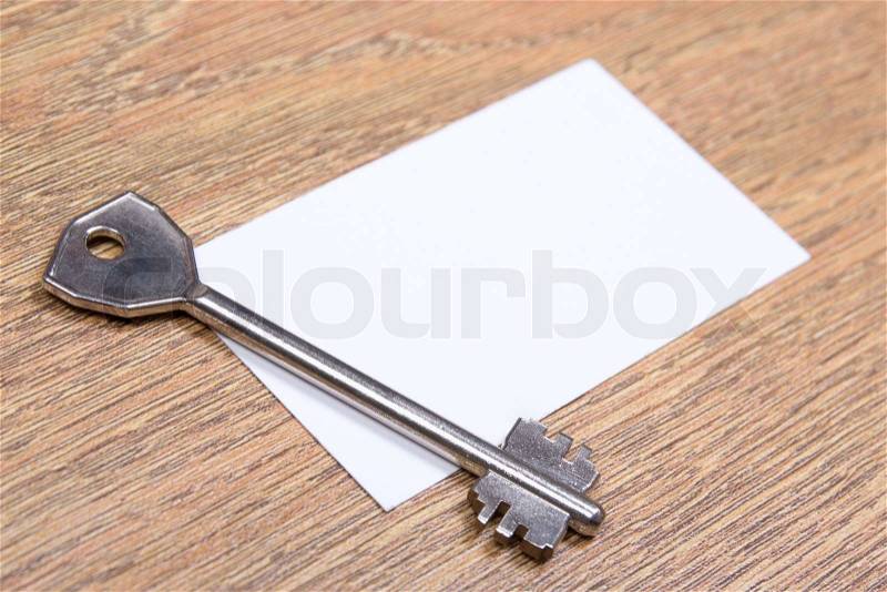 Close up of metal key and visiting card on wooden desktop, stock photo