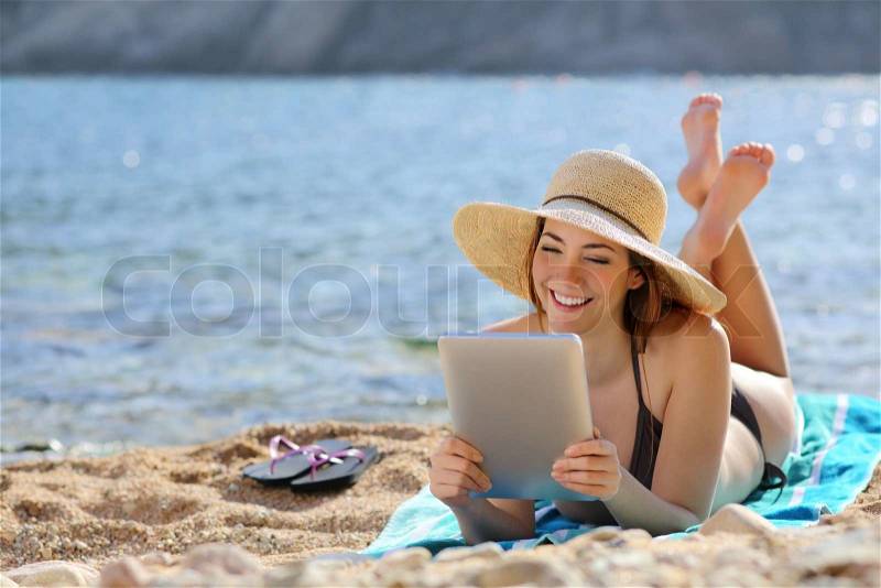 Pretty woman reading a tablet reader on the beach on vacations with the sea in the background , stock photo