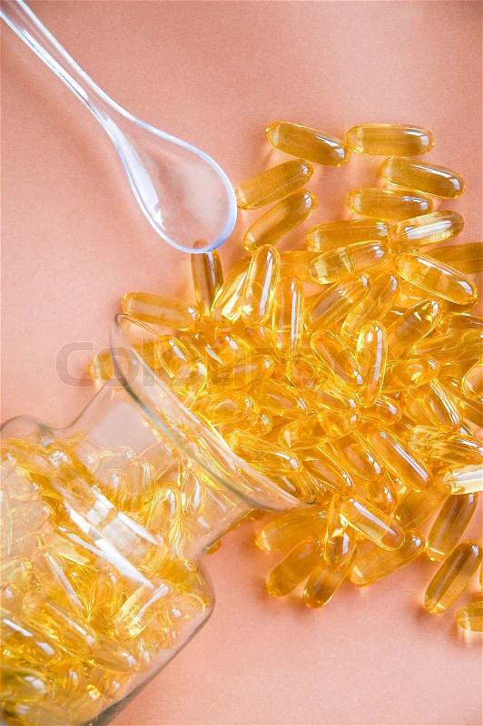 Fish oil capsules splash from glass bottle and spoon beside, stock photo