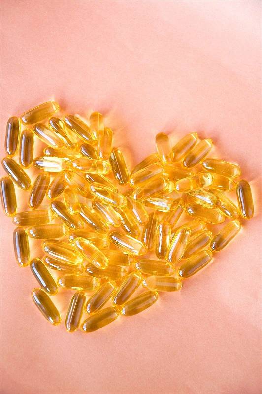 Fish oil capsules in heart shape on pink background, stock photo