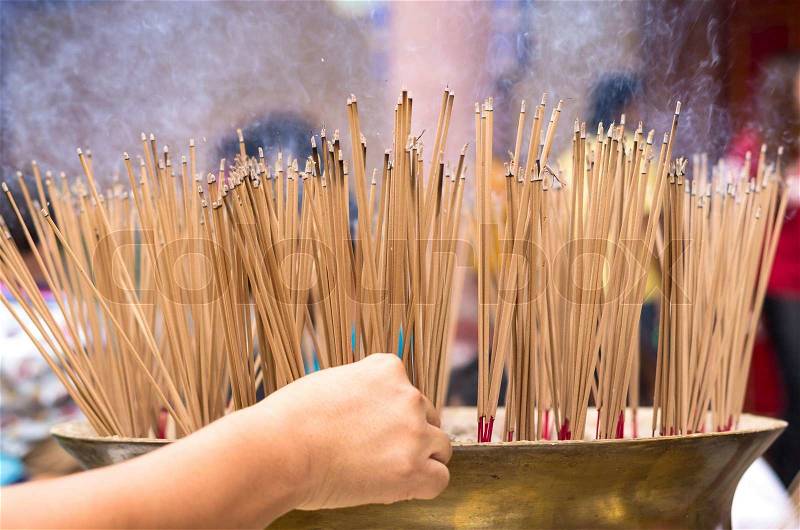 Hand places a stick of incense at a large pot in Chinese temple, stock photo