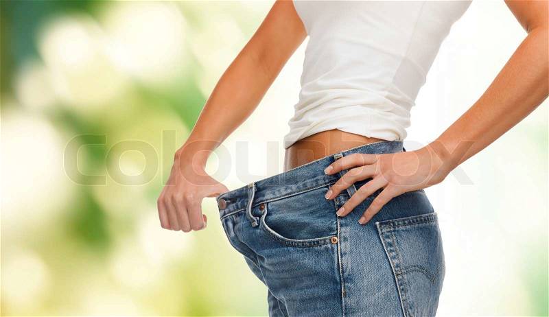 Healthcare, diet and fitness concept - close up of female showing big jeans, stock photo
