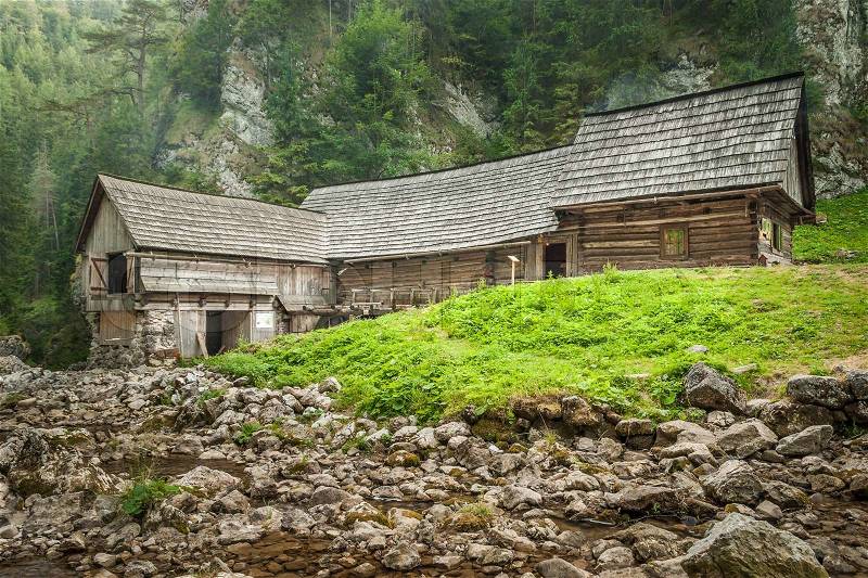 Wooden cottage in the mountains with creek and grass, stock photo