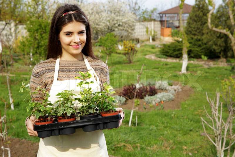 Beautiful smiling woman holding flower plant in garden, stock photo