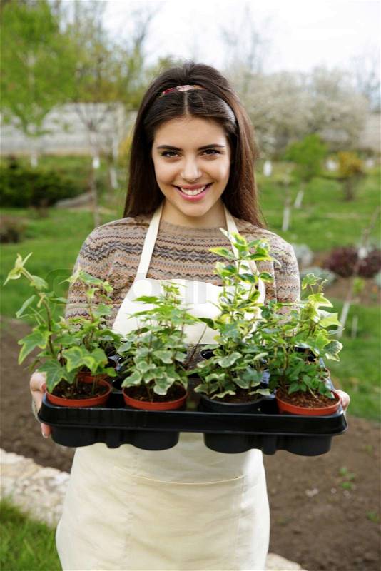 Beautiful happy woman holding flower plant in garden, stock photo