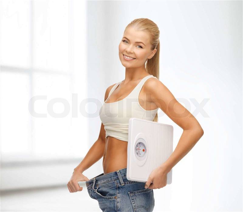 Fitness, diet and healthcare concept - sporty woman showing big pants and holding scales, stock photo