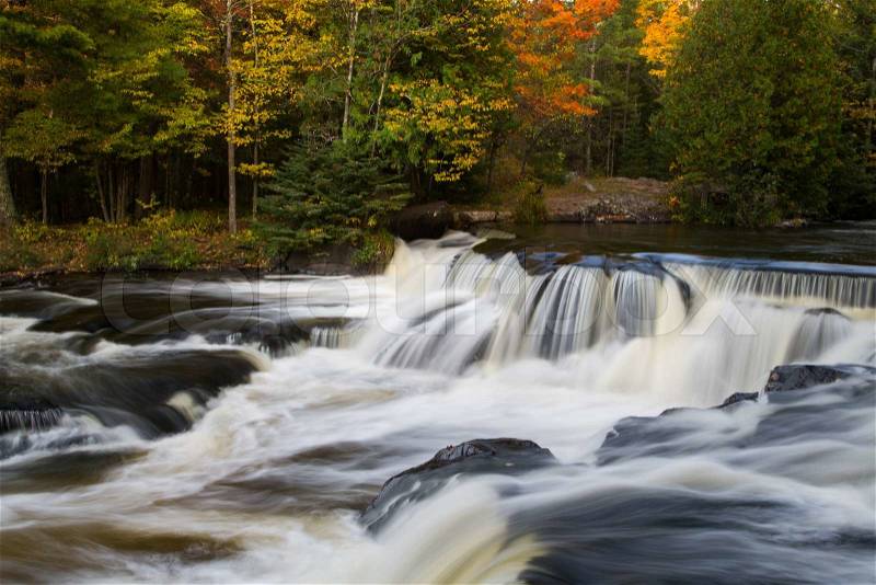 Whitewater flows over dark rock ledges with colorful fall foliage all around at Bond Falls in Michigan\'s western Upper Peninsula, stock photo