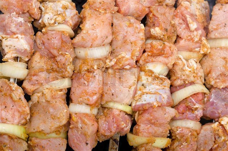 Background of spicy uncooked meat and onion kebabs laid out on a grill ready to be barbecued on a summer picnic, closeup overhead view, stock photo