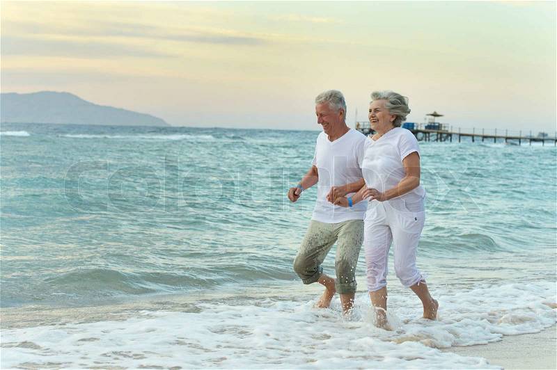 Nice old couple running on sea beach, stock photo