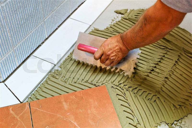 A tiler at work. sticking floor tiles with tile adhesive and trowel, stock photo