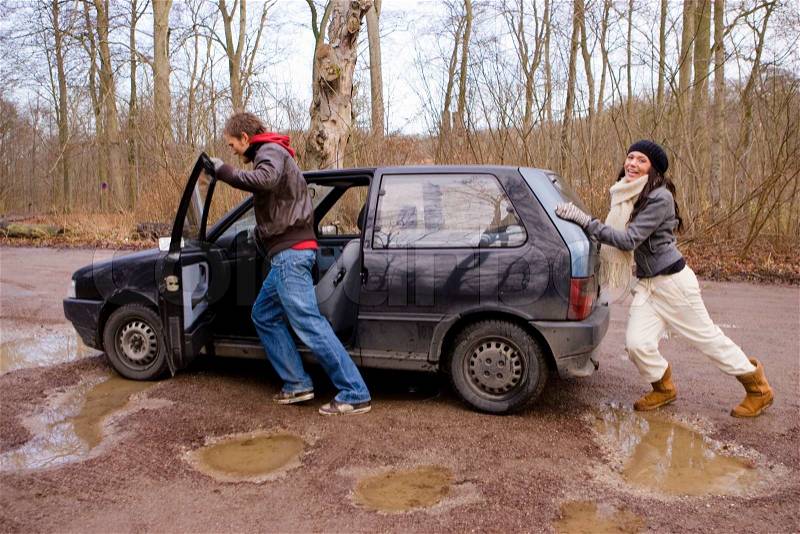 A couple pushing their car that broke down in a muddy field, stock photo