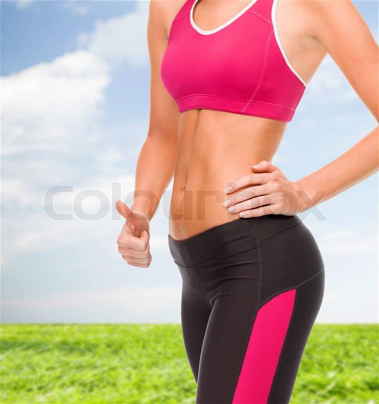 Fitness and diet concept - close up of female abs and hand showing thumbs up, stock photo