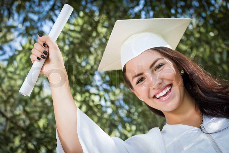 Attractive Mixed Race Girl Celebrating Graduation Outside In Cap and Gown with Diploma in Hand, stock photo