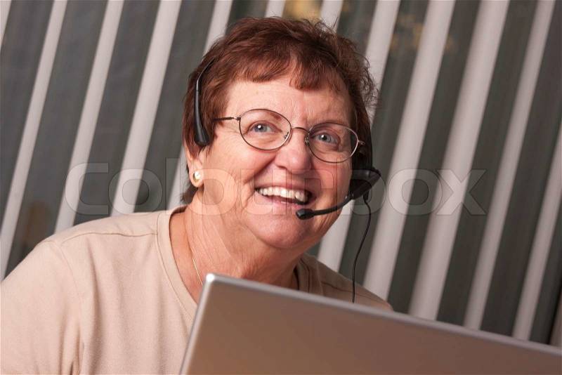 Smiling Senior Adult Woman with Telephone Headset In Front of Computer Monitor, stock photo