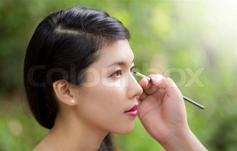 Make-up artist applying bright base color eyeshadow on model\'s eye, stock photo