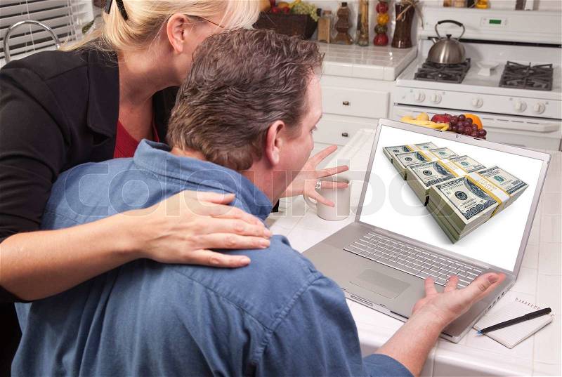 Couple In Kitchen Using Laptop with Stacks of Money on the Screen, stock photo