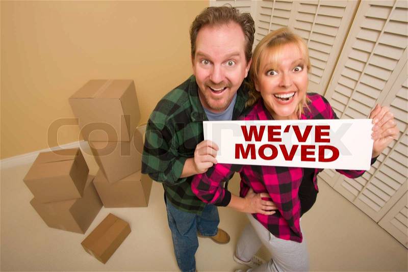 Goofy Couple Holding We\'ve Moved Sign in Room with Packed Cardboard Boxes, stock photo