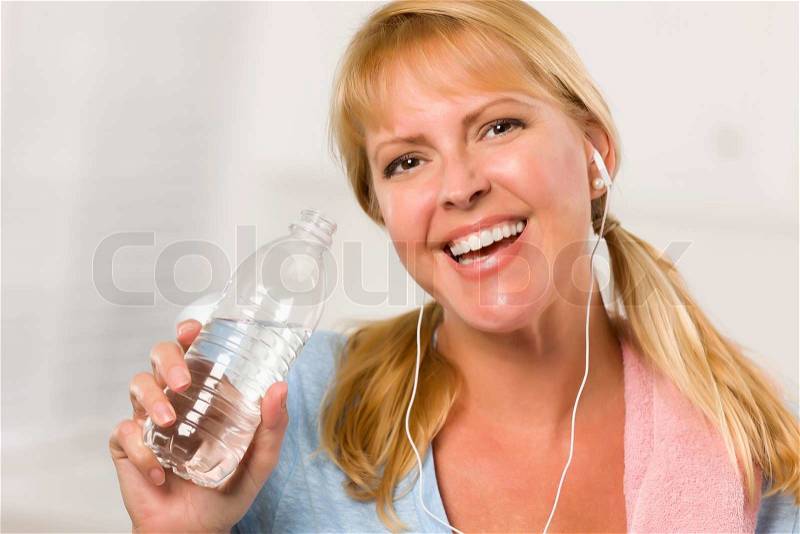 Pretty Blonde Woman with Towel and Ear Phones Drinking From Water Bottle in Her Kitchen, stock photo