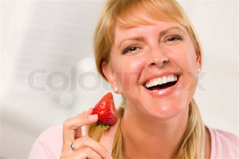 Pretty Smiling Blonde Woman Holding Strawberry in Her Kitchen, stock photo
