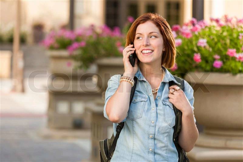 Smiling Young Pretty Female Student with Backpack Walking Outside Using Cell Phone, stock photo